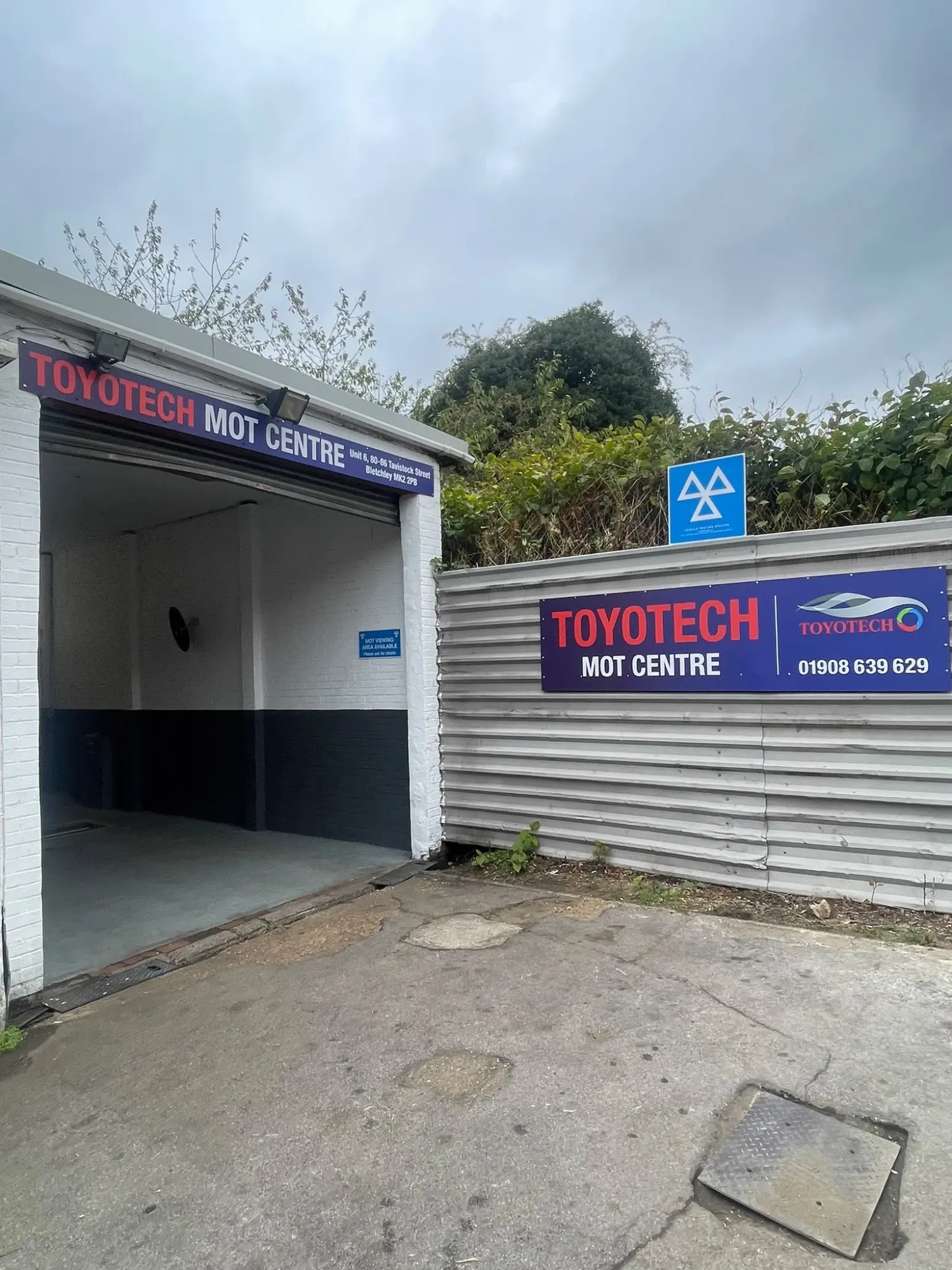 The Toyotech MOT Centre unit at 80-86 Tavistock Street, Bletchley: an open roller-door bay under a blue sign, with a blue MOT testing station sign above the fence beside it